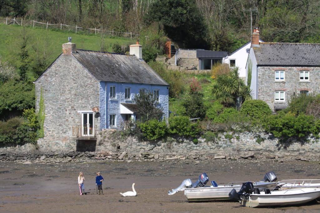 3 cottages in front of South Pool estuary with the tide out and two kids playing next to speed boats