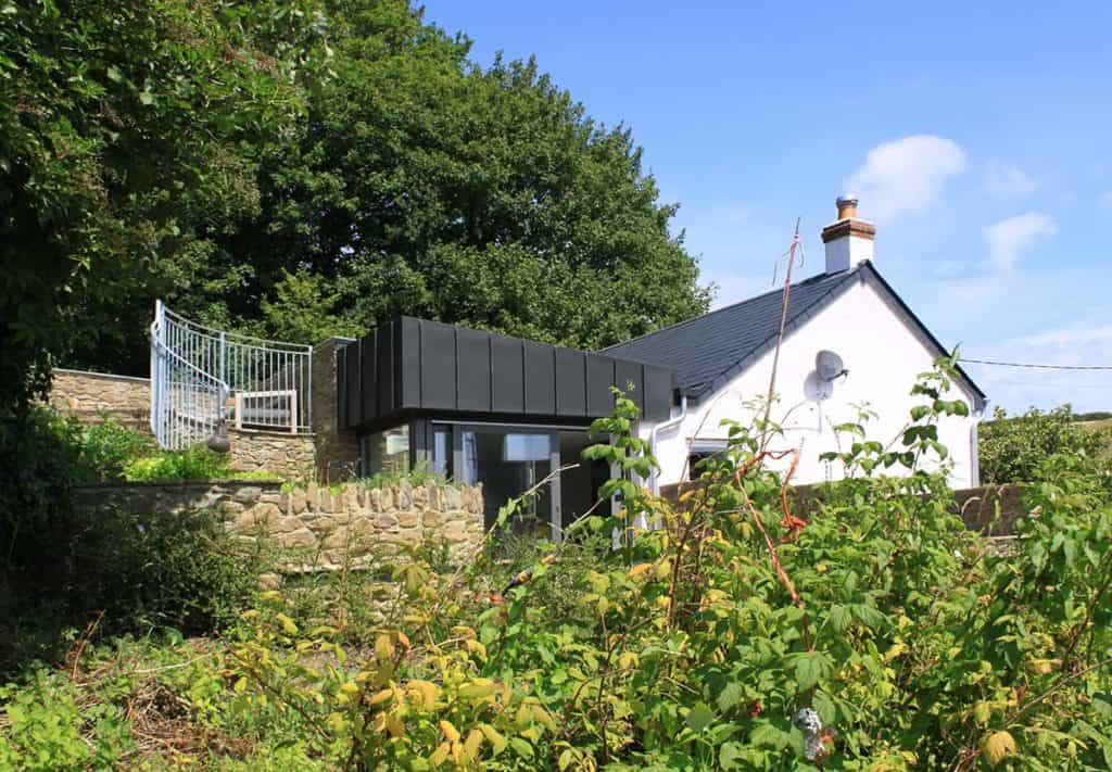 Modern small extension to cottage set in a hill with steps coming down from the road and roof