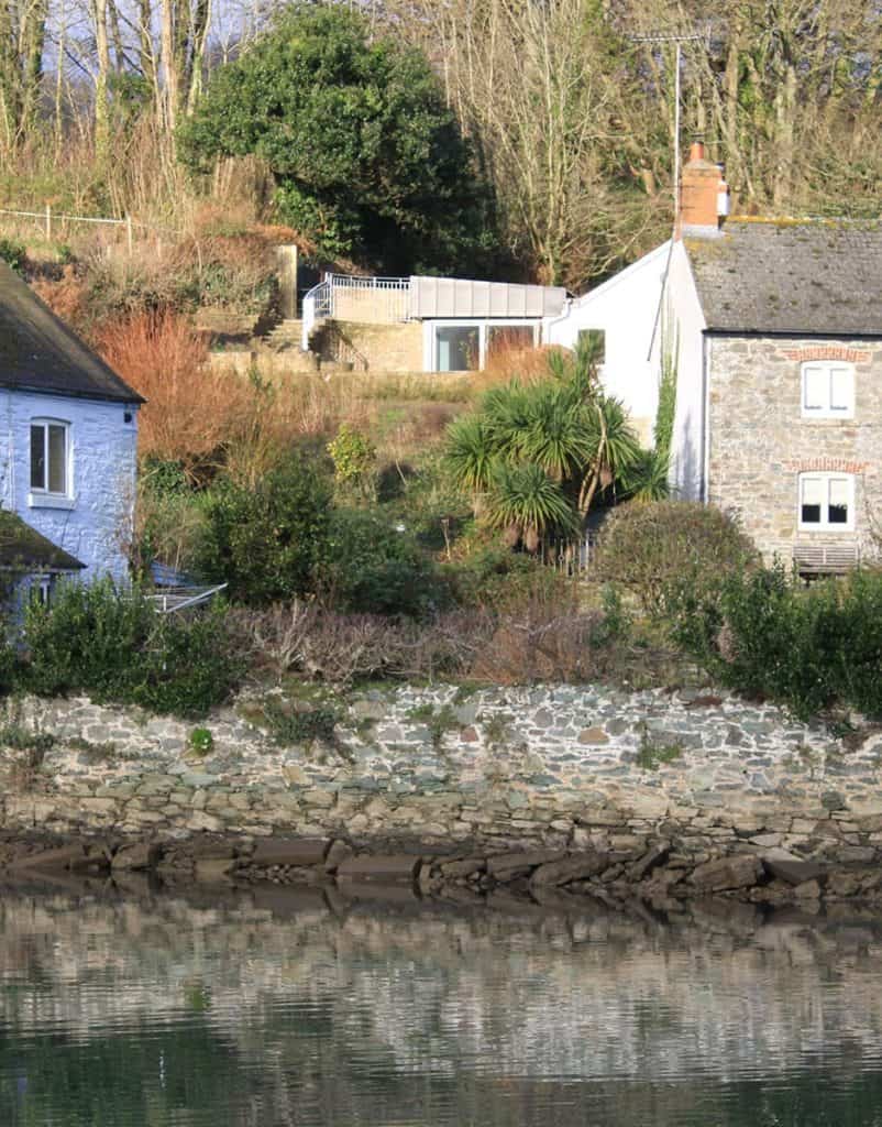 Extension of cottage set in cliff with steps leading down to back of cottage and estuary in the foreground