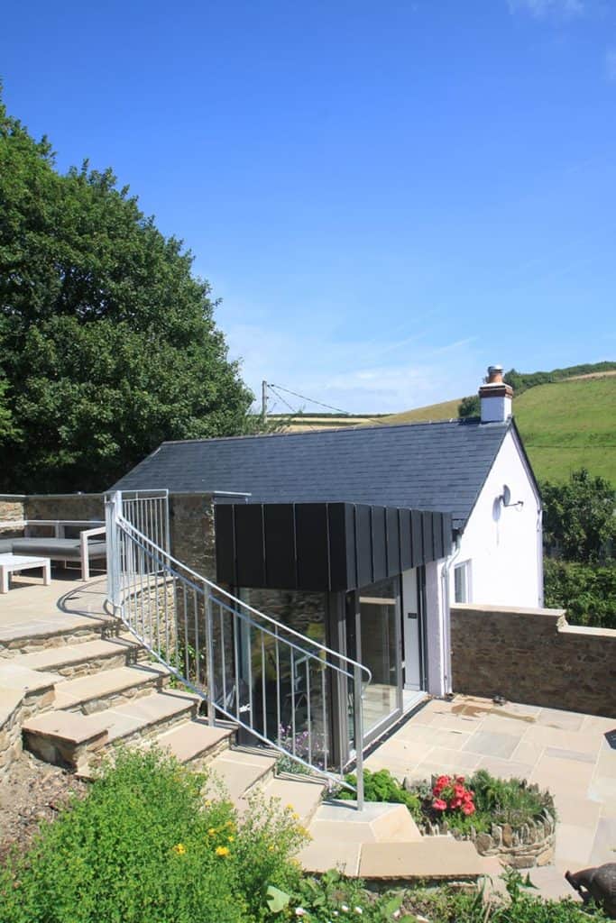 Stone walled steps from patio on top of roof leading down to back of modern extension of old cottage